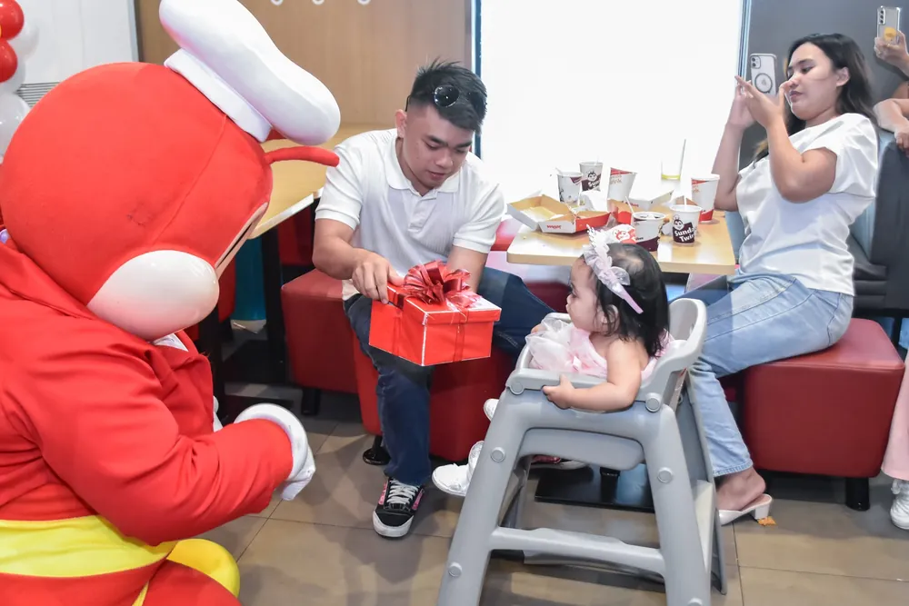 Mascot and parents helping a baby open a gift at a birthday party
