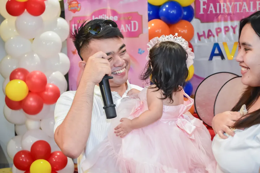 Dad holding a toddler in a pink dress during a birthday toast