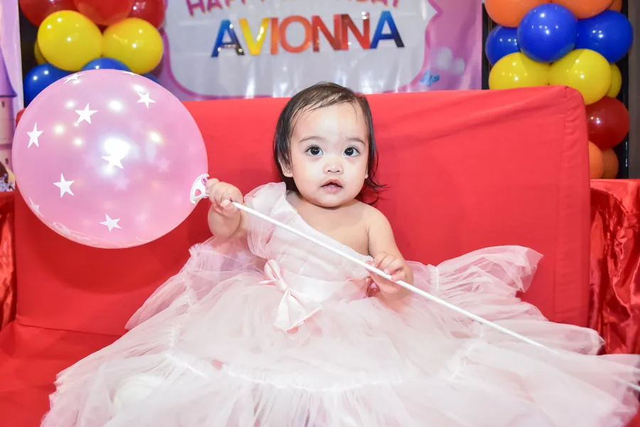 Toddler in a tulle dress holding a pink balloon, birthday portrait
