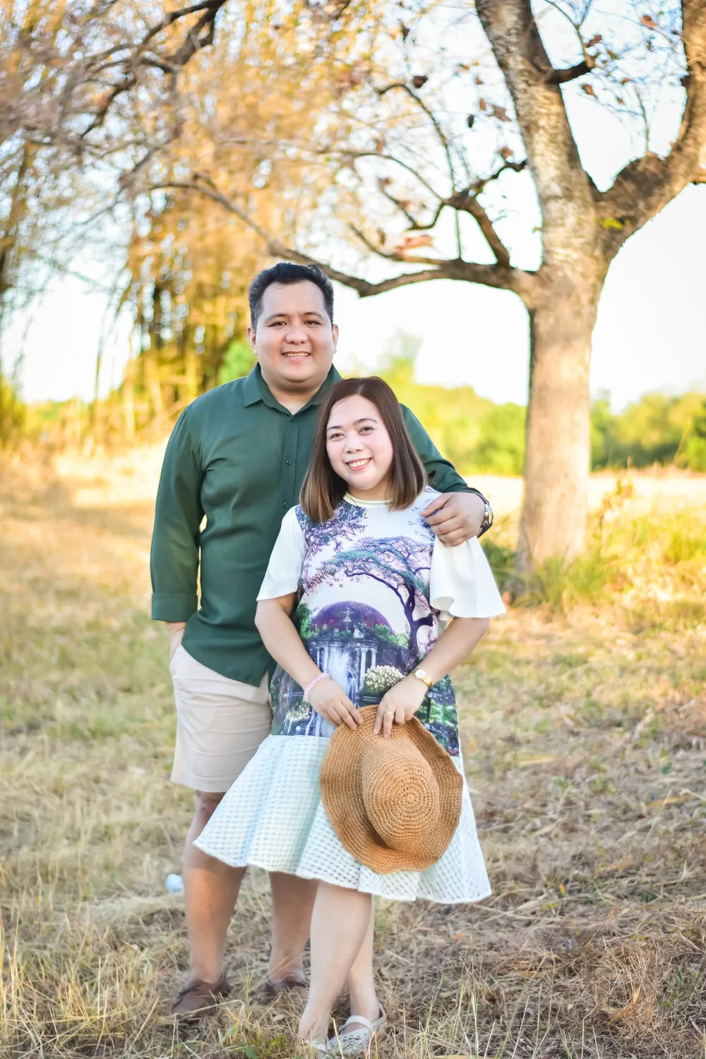 Father and mother posing together under a tree in golden light, outdoor couple portrait